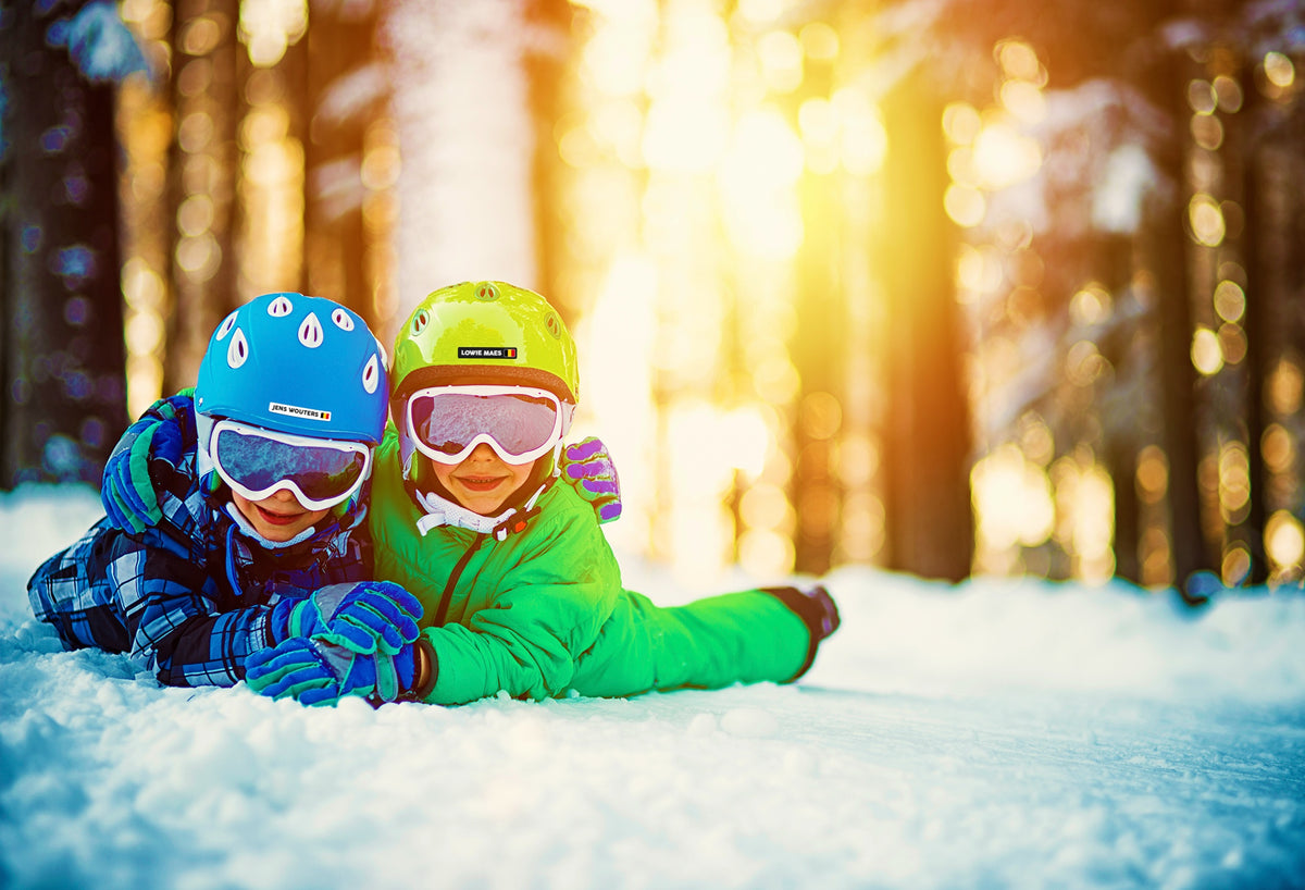 Twee kinderen in de sneeuw met een naamsticker en Belgische vlag op hun skihelm