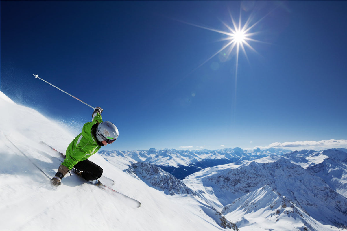 Skiër met groene naamsticker op zijn helm daalt af in de zon, met bergen op de achtergrond