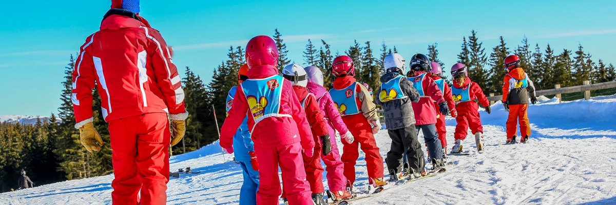 Skischoolgroep kinderen in de rij achter hun skileraar op de piste